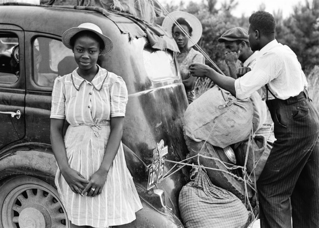 Vintage black and white photo of people preparing for a journey with a classic car.